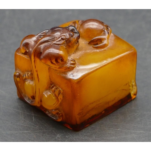 644 - An amber style square seal with raised inset motif, 4cm wide