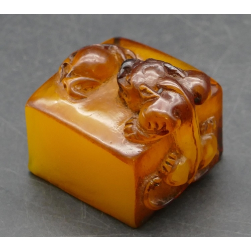 644 - An amber style square seal with raised inset motif, 4cm wide