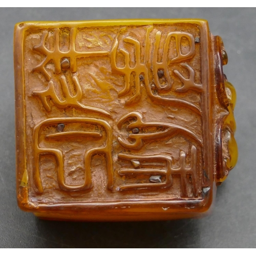 644 - An amber style square seal with raised inset motif, 4cm wide