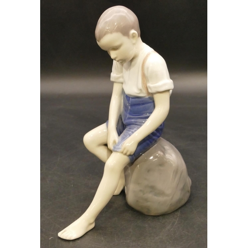 125 - B & G Copenhagen figure of a young boy seated on a rock holding up his trousers, 19.5cm high