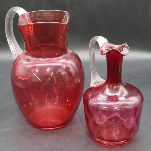 187 - A cranberry glass round bulbous shaped jug with clear reeded handle, 22.5cm high and a smaller cranb... 