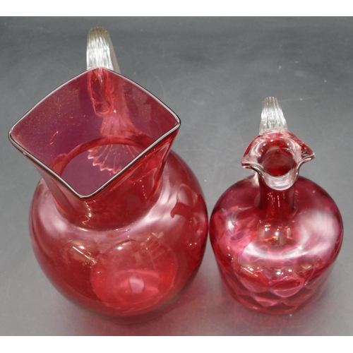 187 - A cranberry glass round bulbous shaped jug with clear reeded handle, 22.5cm high and a smaller cranb... 