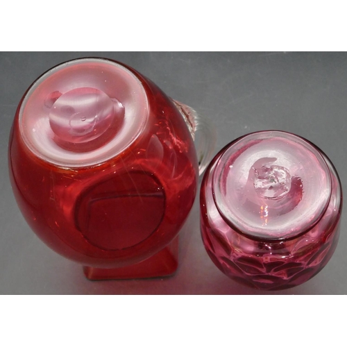 187 - A cranberry glass round bulbous shaped jug with clear reeded handle, 22.5cm high and a smaller cranb... 