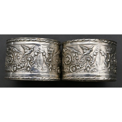 230 - A pair of Continental silver coloured metal large round napkin rings with allover embossed bird, flo... 