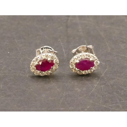 660 - A pair of 18ct white gold oval ruby earrings surrounded by small diamond chips, 1.4 grams gross