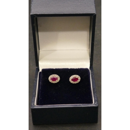 660 - A pair of 18ct white gold oval ruby earrings surrounded by small diamond chips, 1.4 grams gross