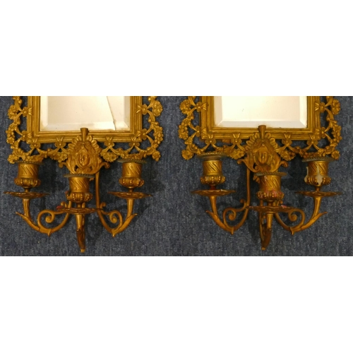 904 - A pair of gilt metal hanging bevelled mirrored wall sconces with allover embossed and pierced figure... 