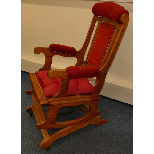 960 - An oak American rocking chair with red overstuffed and studded seat and back with padded arms, on ca... 