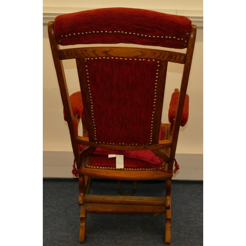 960 - An oak American rocking chair with red overstuffed and studded seat and back with padded arms, on ca... 