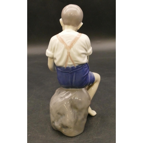 125 - B & G Copenhagen figure of a young boy seated on a rock holding up his trousers, 19.5cm high