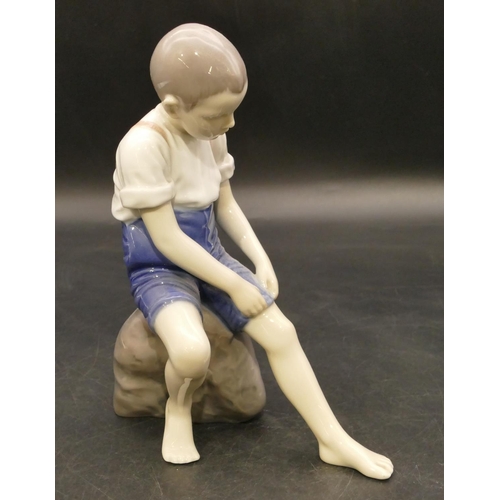 125 - B & G Copenhagen figure of a young boy seated on a rock holding up his trousers, 19.5cm high