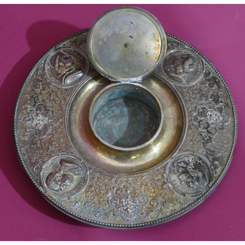 174 - A silver plated round inkwell with hinged circular lid and allover embossed figurehead, cupid, flora... 