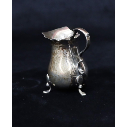 232 - A small silver bulbous shaped cream jug with crinkled rim, scroll handle on splayed feet, 7.5cm high... 