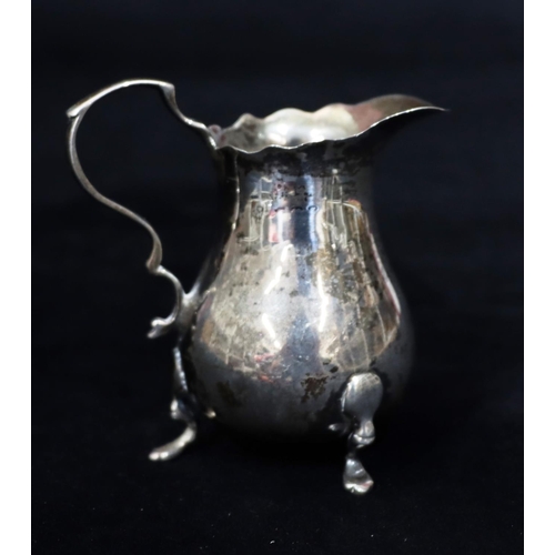 232 - A small silver bulbous shaped cream jug with crinkled rim, scroll handle on splayed feet, 7.5cm high... 