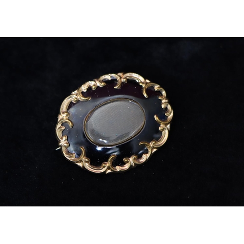 347 - A Victorian oval black enamelled mourning brooch with raised scroll decoration, 5cm wide