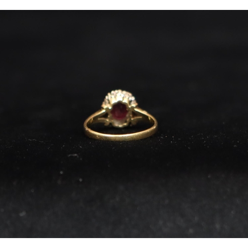 550 - An 18ct gold ladies' cluster ring set with centre oval ruby surrounded by small diamond chips, Size ... 