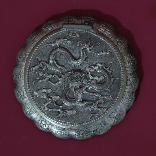 561 - An Oriental silver coloured metal round scallop shaped compact with raised dragon decoration, hinged... 