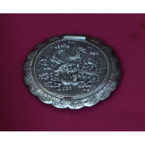 566 - An Oriental silver coloured metal round scallop shaped compact with raised dragon decoration, hinged... 