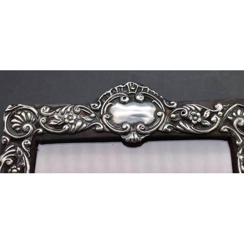 324 - A Birmingham silver mounted freestanding photograph frame with embossed floral, leaf and scroll deco... 