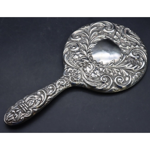 325 - A Birmingham silver mounted hand mirror with allover embossed figurehead, floral, leaf and scroll de... 