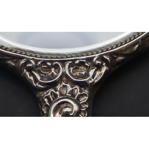 325 - A Birmingham silver mounted hand mirror with allover embossed figurehead, floral, leaf and scroll de... 