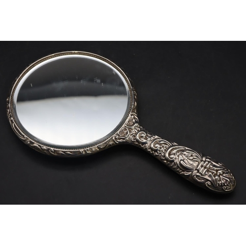 325 - A Birmingham silver mounted hand mirror with allover embossed figurehead, floral, leaf and scroll de... 