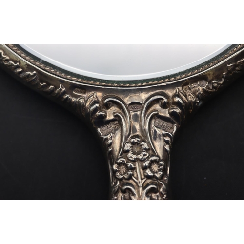 327 - A Birmingham silver hand mirror with embossed cupid, floral and scroll decoration