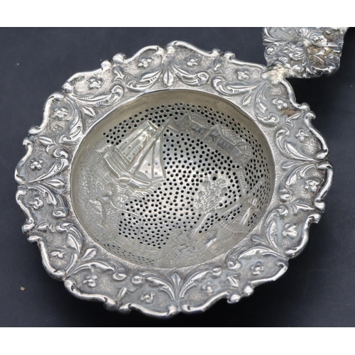 328 - A Continental silver coloured metal tea strainer with embossed ship, windmill, floral and scroll dec... 