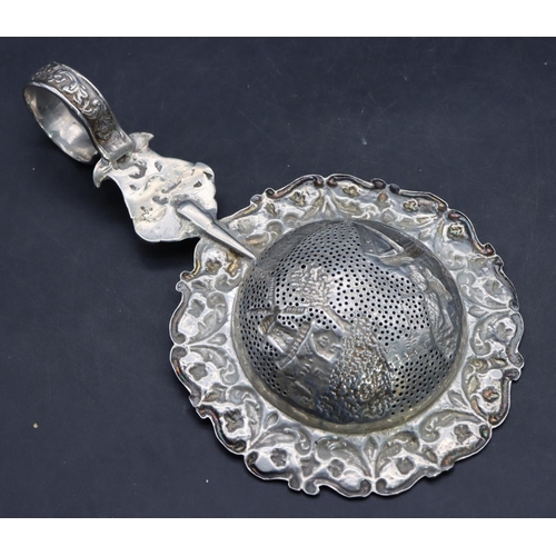 328 - A Continental silver coloured metal tea strainer with embossed ship, windmill, floral and scroll dec... 