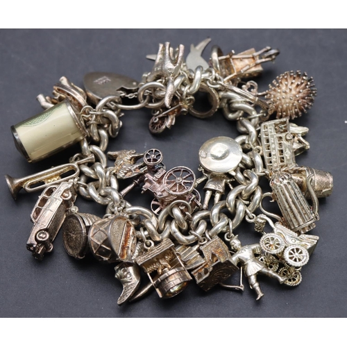 540 - A silver charm bracelet with padlock clasp mounted with 26 charms, 140.6 grams