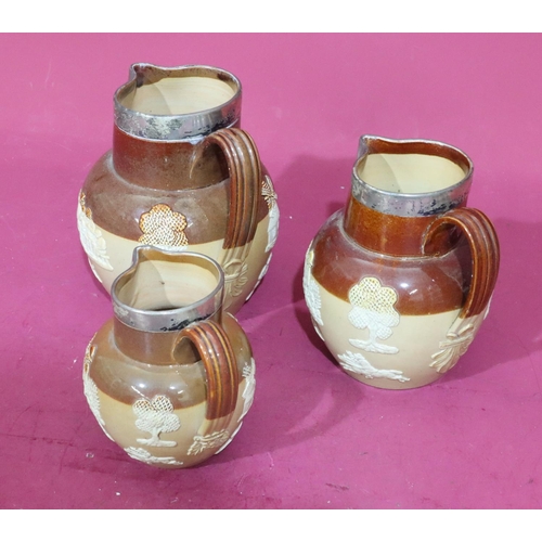 87 - A set of 3 Royal Doulton round bulbous thin neck jugs with London silver necks on brown ground with ... 