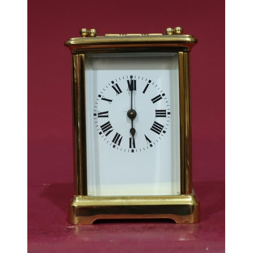 915 - A gilt metal carriage clock with white enamel dial, Roman numerals and swing overhead handle, 12cm h... 