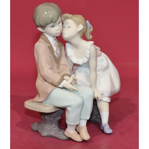 133 - A Lladro group of a young boy and girl sitting on a bench, 20cm high