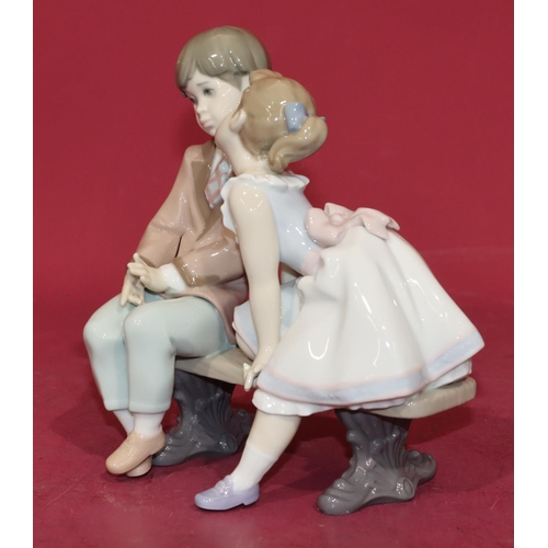 133 - A Lladro group of a young boy and girl sitting on a bench, 20cm high