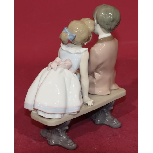 133 - A Lladro group of a young boy and girl sitting on a bench, 20cm high