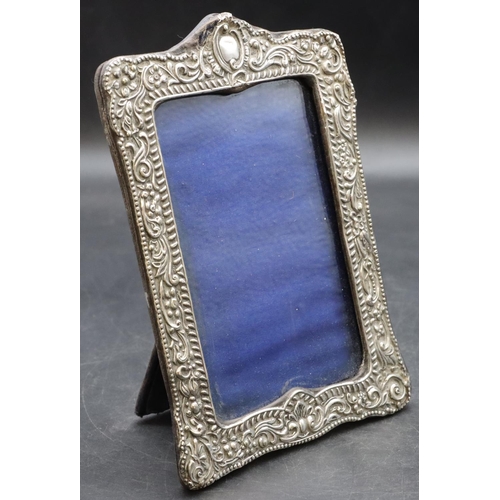 259 - A silver mounted freestanding photograph frame with embossed floral, leaf and scroll rim (slight dam... 