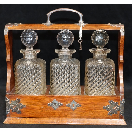 728 - An oak 3-bottled tantalus with silver plated handle and mounts, set with 3 cut glass square decanter... 