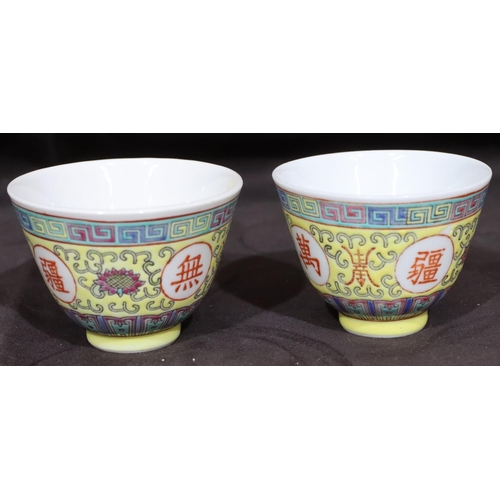 132 - A pair of Oriental tea bowls on yellow ground with coloured key pattern, scroll and floral decoratio... 