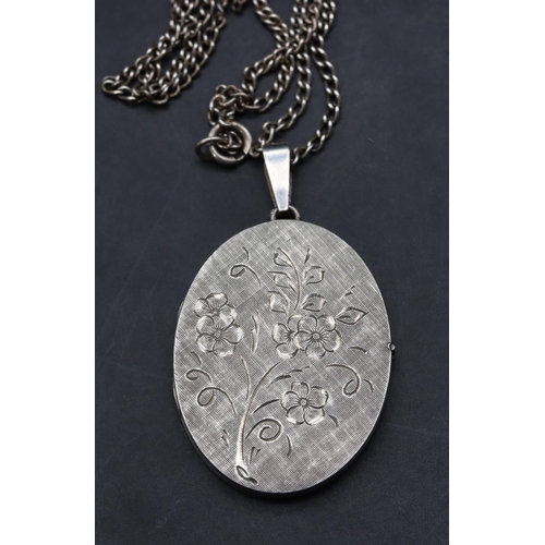 417 - A silver oval locket with engraved floral hinged front, with chain, 19.5 grams