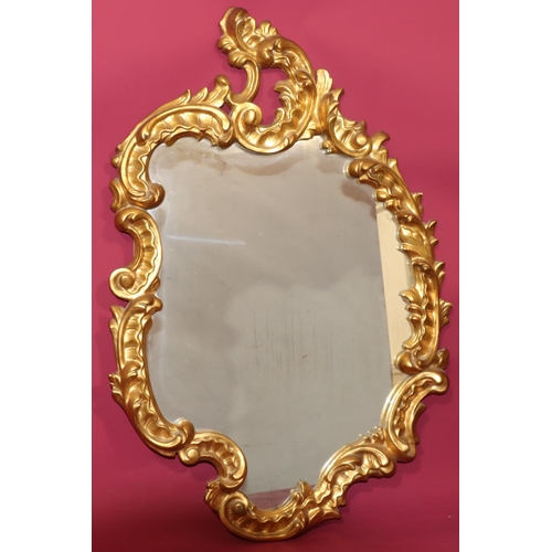 820 - A 20th Century carved giltwood scallop shaped hanging wall mirror with raised leaf and scroll decora... 