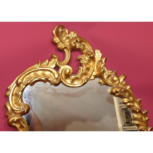 820 - A 20th Century carved giltwood scallop shaped hanging wall mirror with raised leaf and scroll decora... 