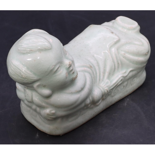 51 - An Oriental glazed earthenware pillow in the form of a child on pale green ground, 20cm long