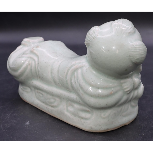 51 - An Oriental glazed earthenware pillow in the form of a child on pale green ground, 20cm long