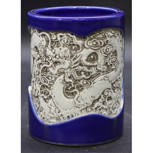 57 - An Oriental cylindrical brush pot on blue ground with inserted white dragon decoration, 14cm high