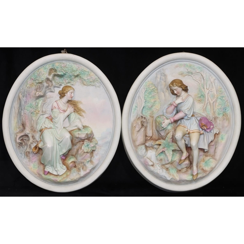 58 - A pair of oval Bisque hanging plaques with raised figures of a seated young gentleman and lady (lady... 