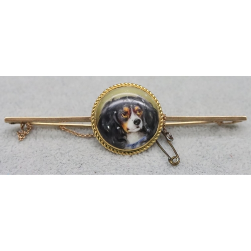 612 - A 9ct gold bar brooch with centre circular china plaque depicting figurehead of a King Charles spani... 