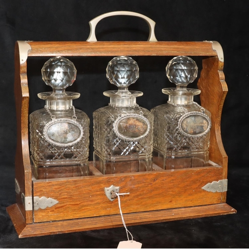 766 - An oak tantalus containing 3 square cut glass decanters (1 cracked and 2 chipped), with 3 silver pla... 