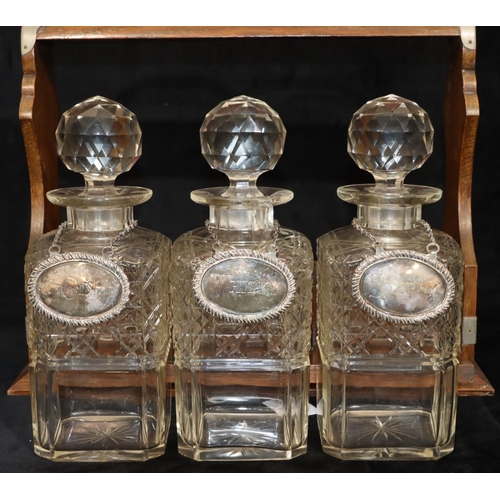 766 - An oak tantalus containing 3 square cut glass decanters (1 cracked and 2 chipped), with 3 silver pla... 