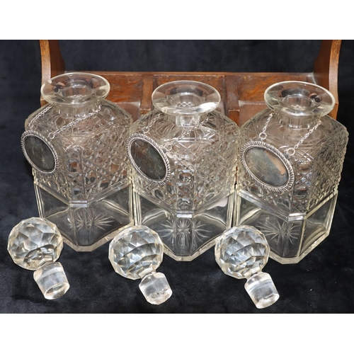 766 - An oak tantalus containing 3 square cut glass decanters (1 cracked and 2 chipped), with 3 silver pla... 