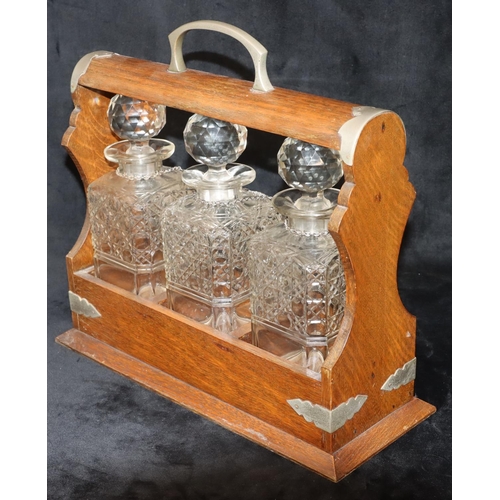 766 - An oak tantalus containing 3 square cut glass decanters (1 cracked and 2 chipped), with 3 silver pla... 